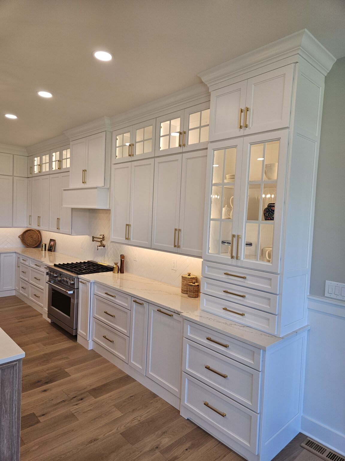 Integrity Cabinets white shaker cabinetry with glass-front stacker cabinets, interior accent lighting, and brushed brass pulls.