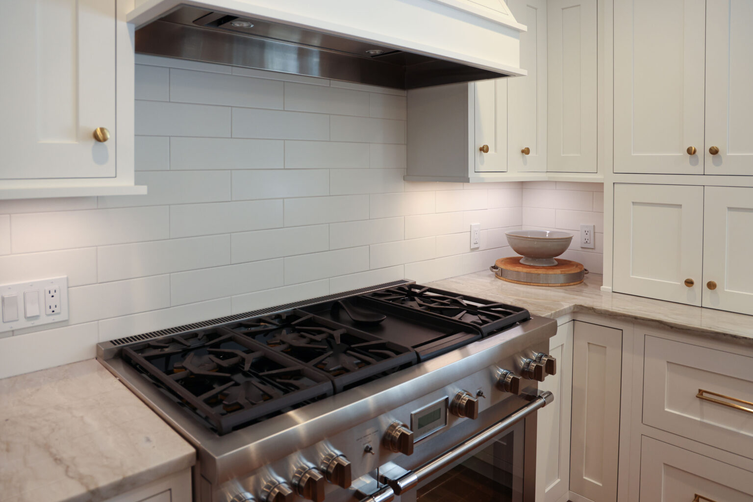 Custom white Brighton Cabinetry inset kitchen featuring brushed brass hardware, a white subway tile backsplash, and a professional-grade stainless steel range.