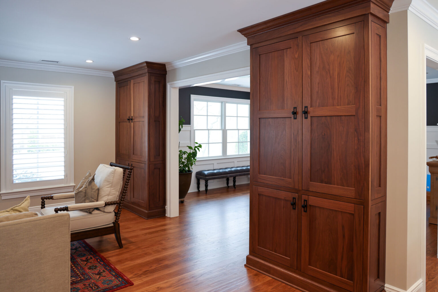Custom rich wood Brighton cabinetry tall pantry cabinets with black hardware flanking an arched doorway, featuring natural hardwood floors and crown molding.