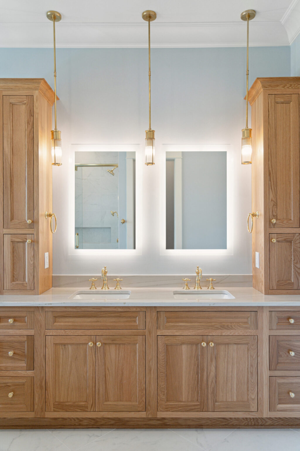 Integrity Cabinets custom double vanity with natural oak shaker cabinetry, dual sink marble countertop, and brass pendant lights.