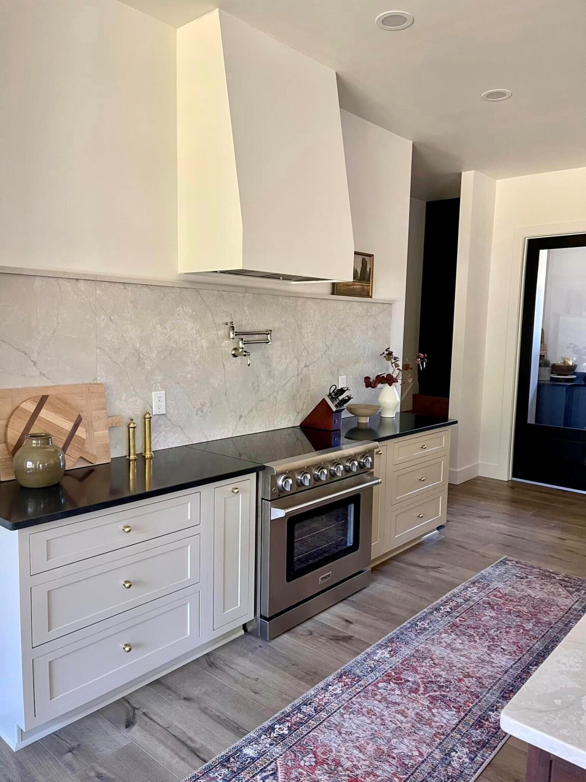 Integrity Cabinets cream inset base cabinets with brass hardware, black countertops, and modern range hood.