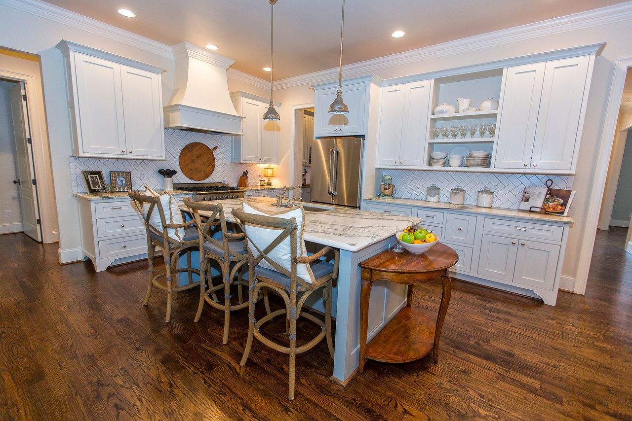 Integrity Cabinets white shaker custom kitchen featuring a marble island, custom range hood, and open display shelving